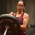 Woman lifting a barbell with weights in a gym setting wearing Athlos Women's Agile Singlet