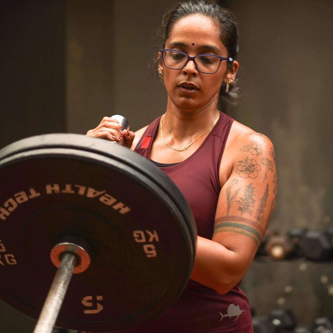 Woman lifting a barbell with weights in a gym setting wearing Athlos Women's Agile Singlet
