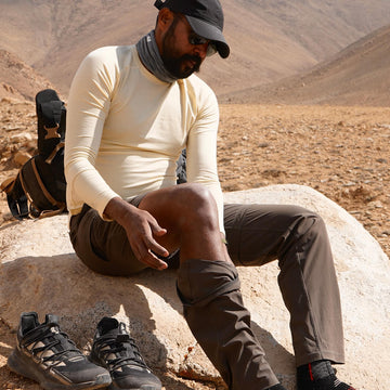 Man sitting on a rock in a desert landscape with hiking shoes beside him wearing Athlos Convertible Pants