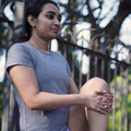 Woman in a gray Athlos Distane t-shirt sitting outdoors with trees in the background