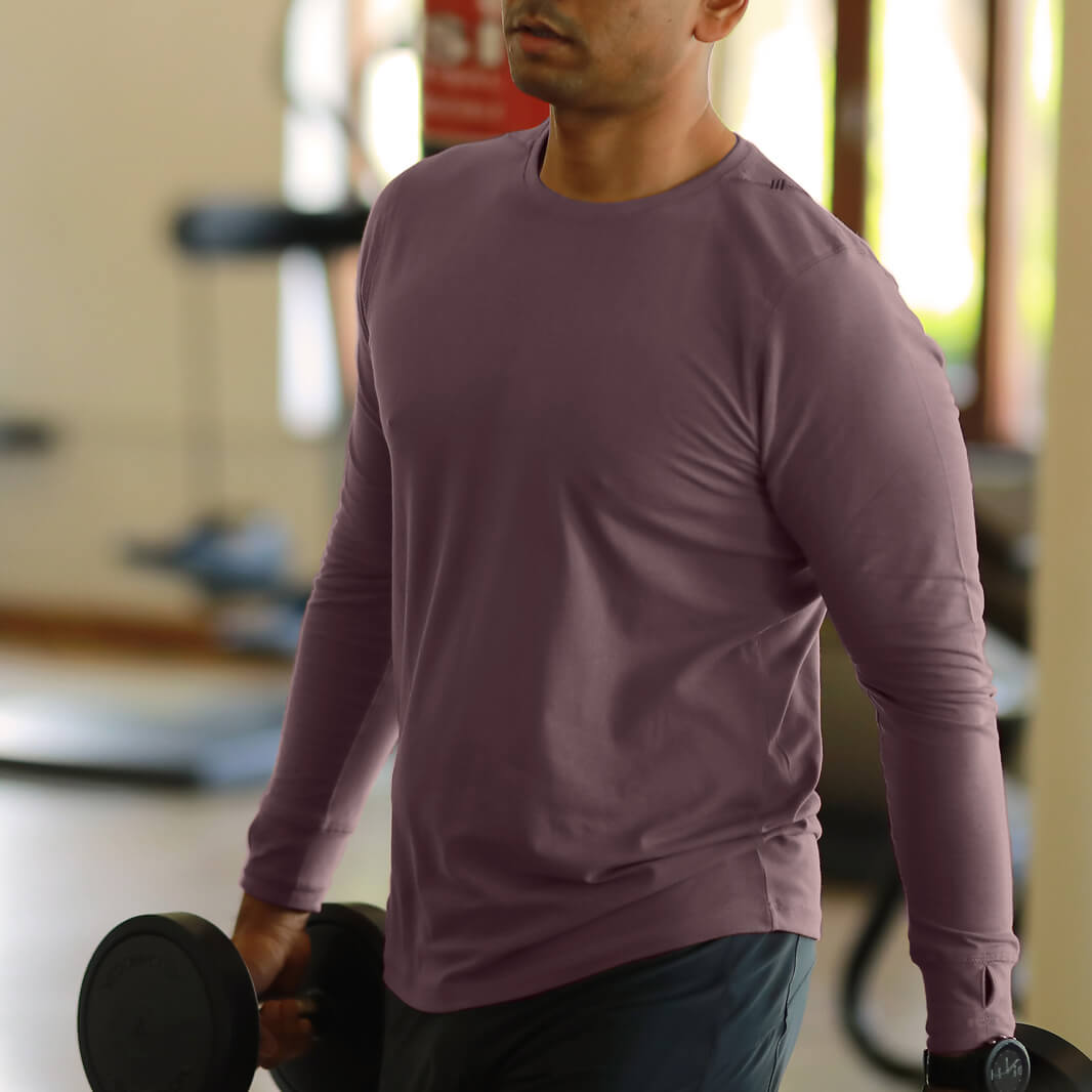 Man in a gym wearing a purple long-sleeve shirt holding a dumbbell.