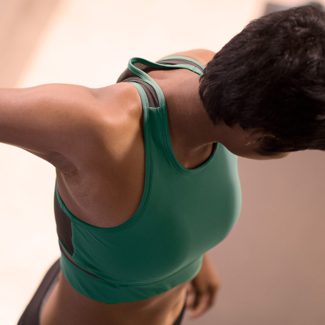Women wearing a green Athlos Mid Intensity bra with a neutral background