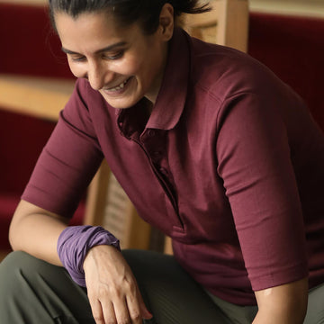Person wearing a maroon Athlos Polo t-shirt and purple wristband sitting on a red couch.
